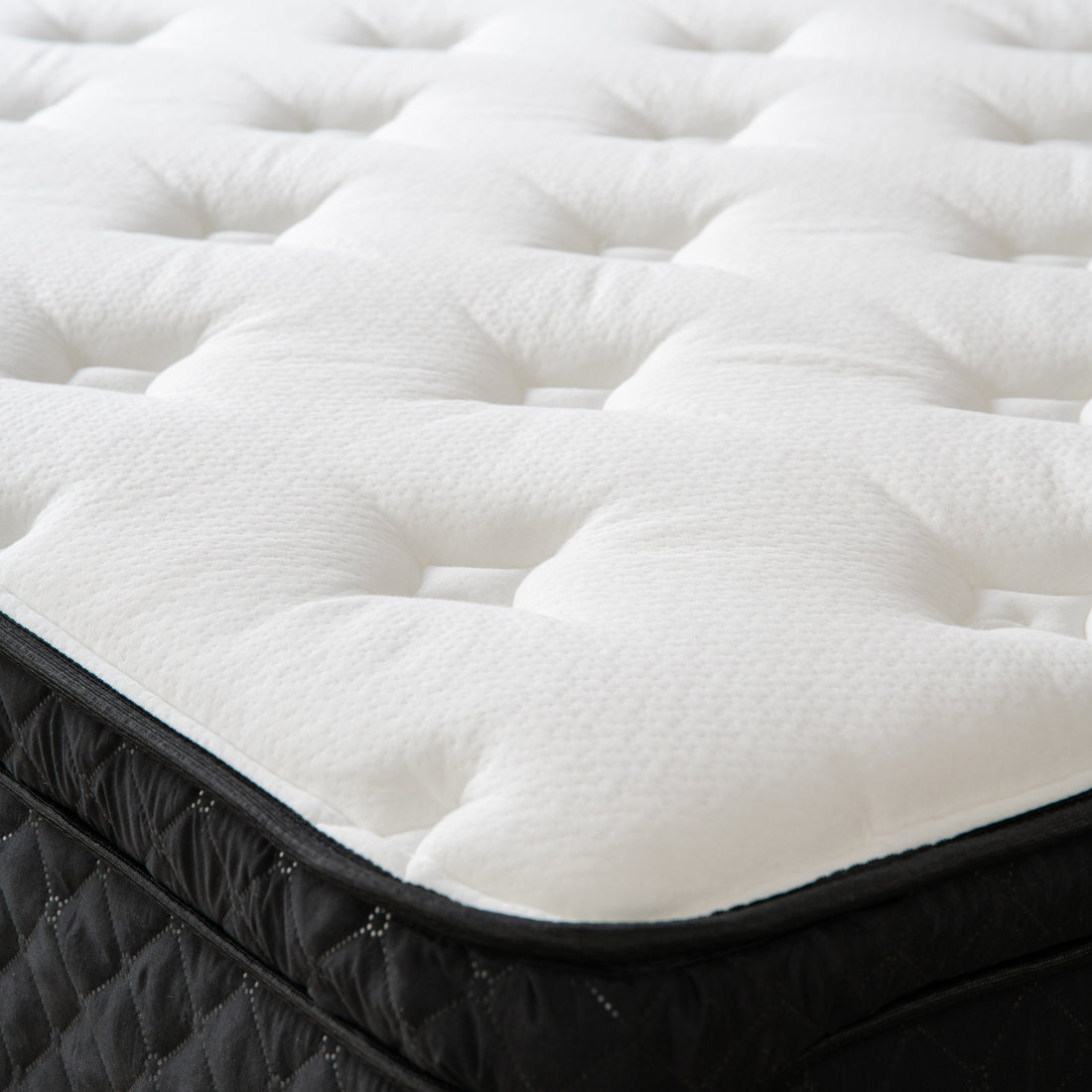 Close-up of the white quilted top and black side panel of a bare Hamuq mattress with no bedding