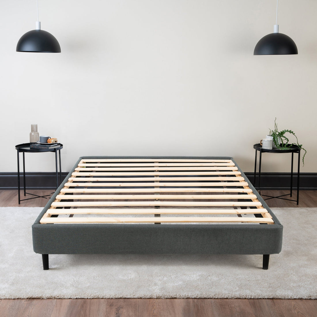 Empty upholstered platform bed frame with wooden slats and a centre support rail, in a bedroom with two side tables