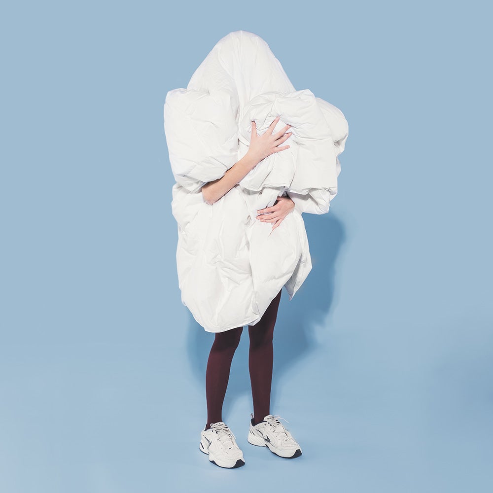 A person holding a large white Hamuq down duvet bundled in their arms against a blue background