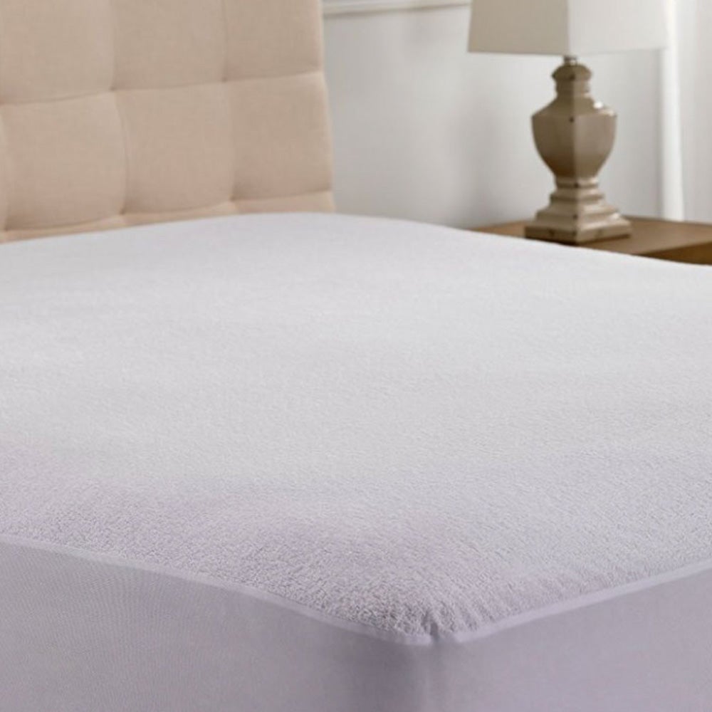 White Hamuq mattress protector fitted over a mattress in front of a beige upholstered headboard with a bedside lamp