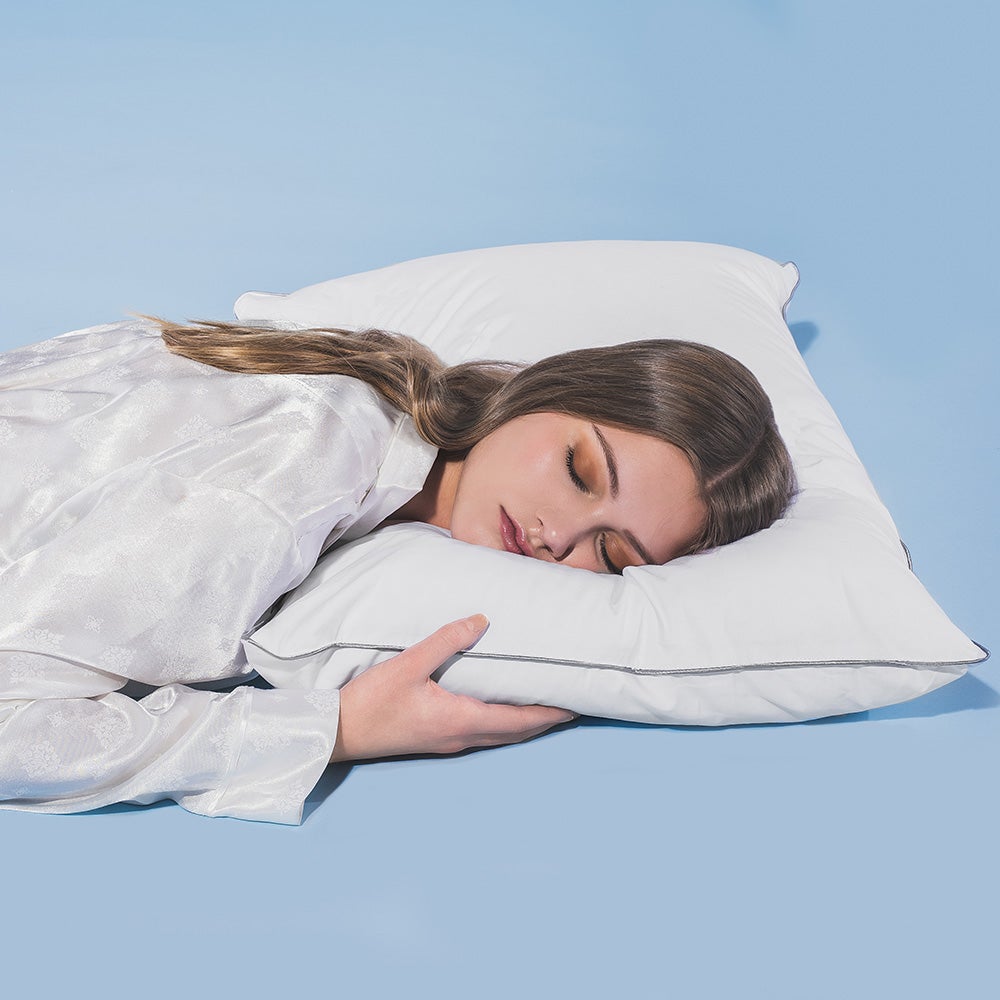 A woman sleeping on her side with her head on a white Hamuq MicroGel pillow against a blue background