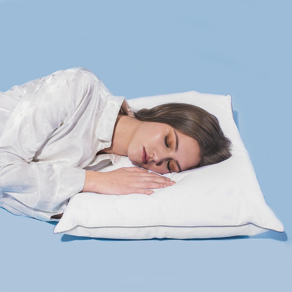 A woman in a white shirt sleeping on her side with her head on a white pillow against a light blue background