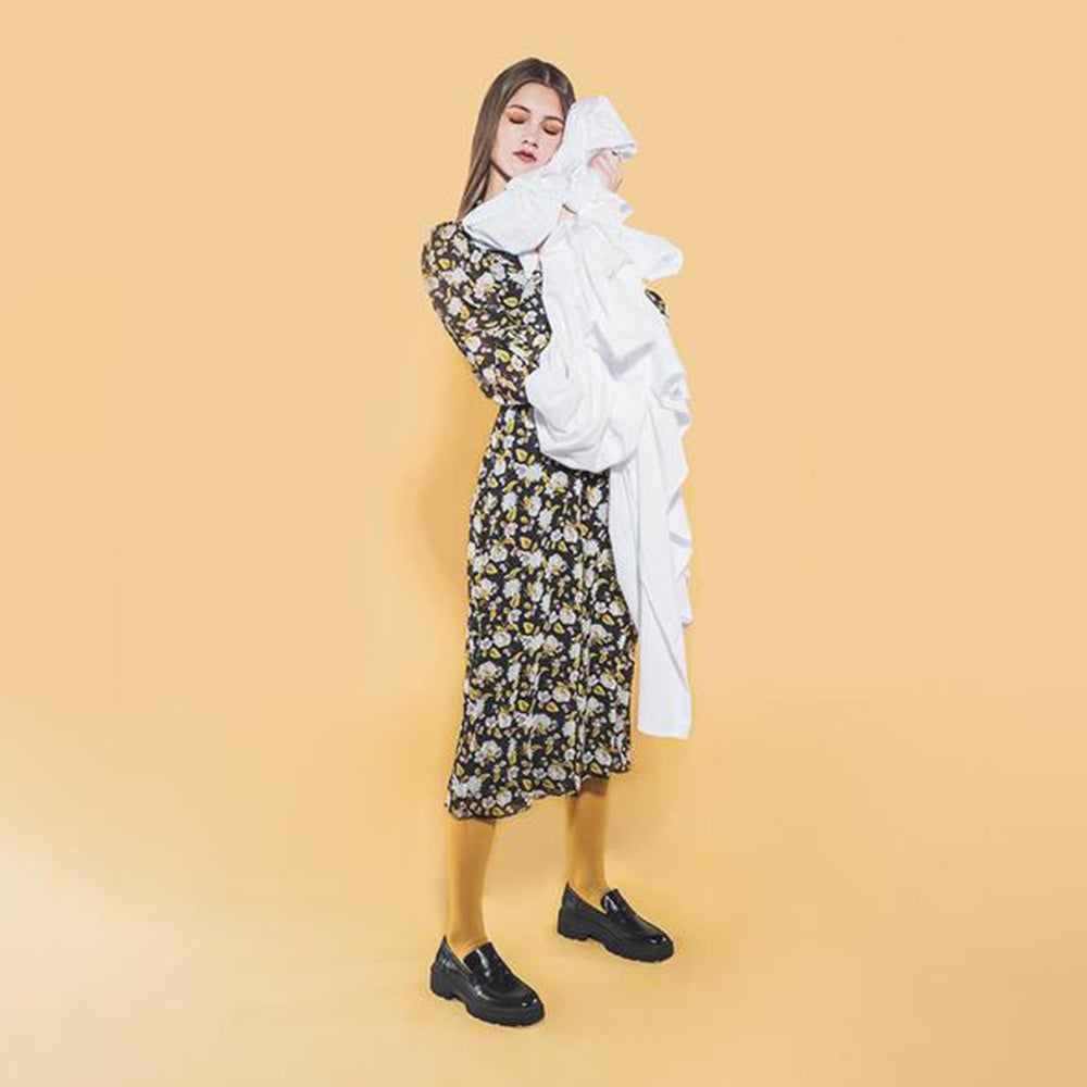 A woman in a floral dress carrying an armful of white bed sheets against a light orange background